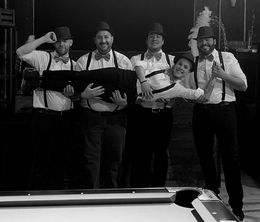 Équipe de traiteurs événementiels en tenue thématique vintage, posant de manière ludique autour d’une table de billard, illustrant l’ambiance conviviale et le professionnalisme lors d’événements.