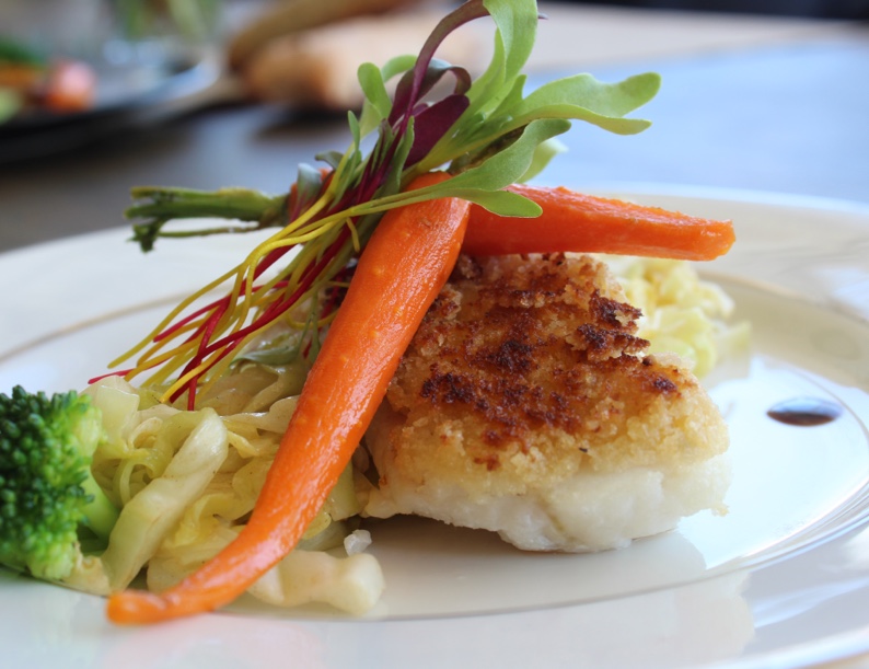 Plat gastronomique raffiné composé de poisson pané, légumes croquants et garniture colorée, préparé par un traiteur événementiel.