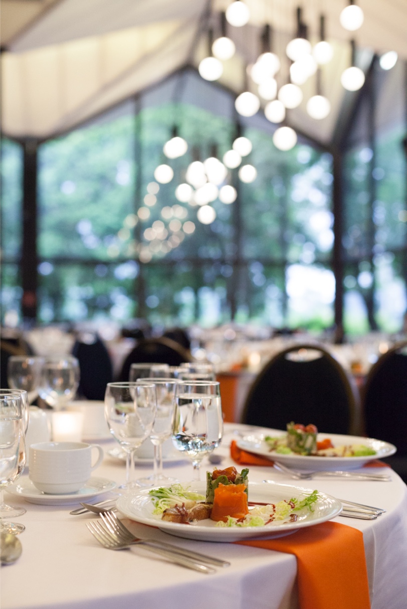 Tables de réception élégamment dressées avec des assiettes garnies et des verres, dans une salle de banquet lumineuse, reflétant le service soigné d’un traiteur événementiel.